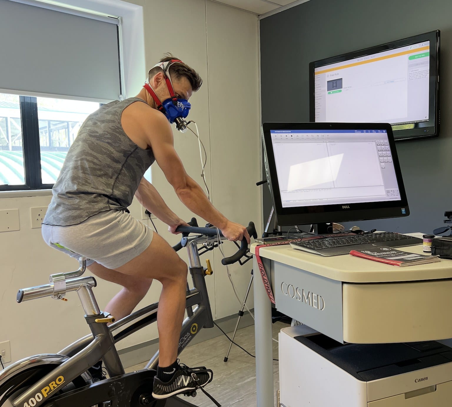 Delano on a cycle ergometer wearing a CPET mask, beside the Cosmed metabolic cart