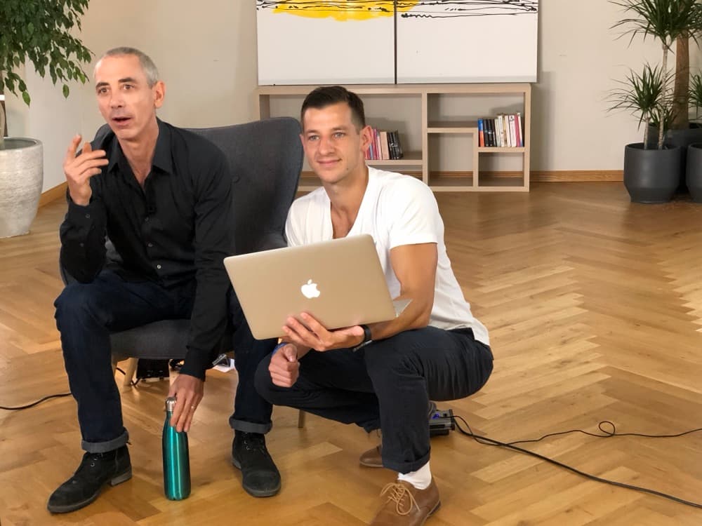 Delano crouching with a laptop beside Steven Kotler at a shoot